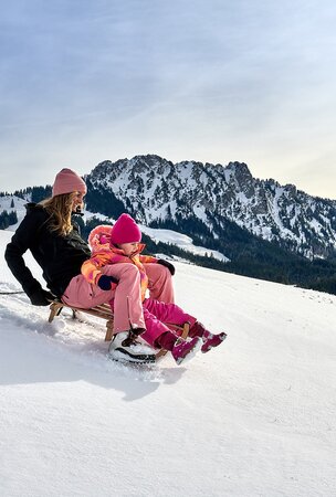 Frau und Kind fahren Schlitten auf verschneitem Berghang
