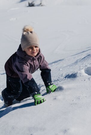 Kleines Kind in Winterkleidung klettert verschneiten Hügel hinauf