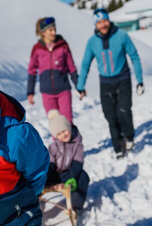 Lachender Junge zieht Schlitten im Schnee mit Familie