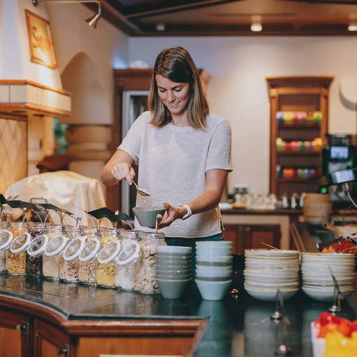 Frau schöpft Müsli am Frühstücksbuffet im Hotel Tyrol Haldensee