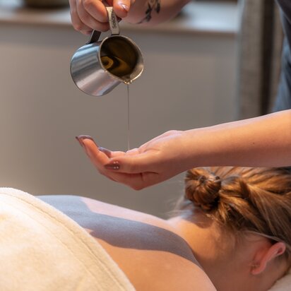 Wellnessanwendung: Öl wird auf den Rücken einer Frau gegossen