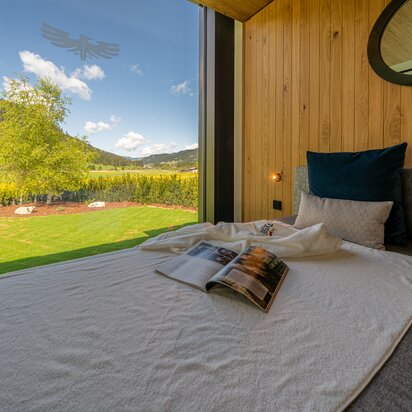 Gemütliches Bett mit Fensterblick auf Wiese und Berge