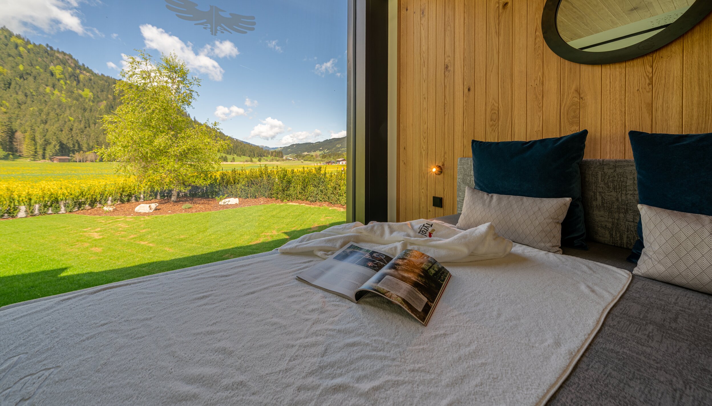 Gemütliches Bett mit Fensterblick auf Wiese und Berge