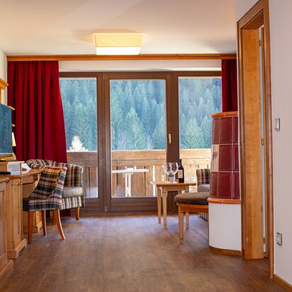 Hotelzimmer mit Holzboden, Kachelofen und Ausblick auf den Wald