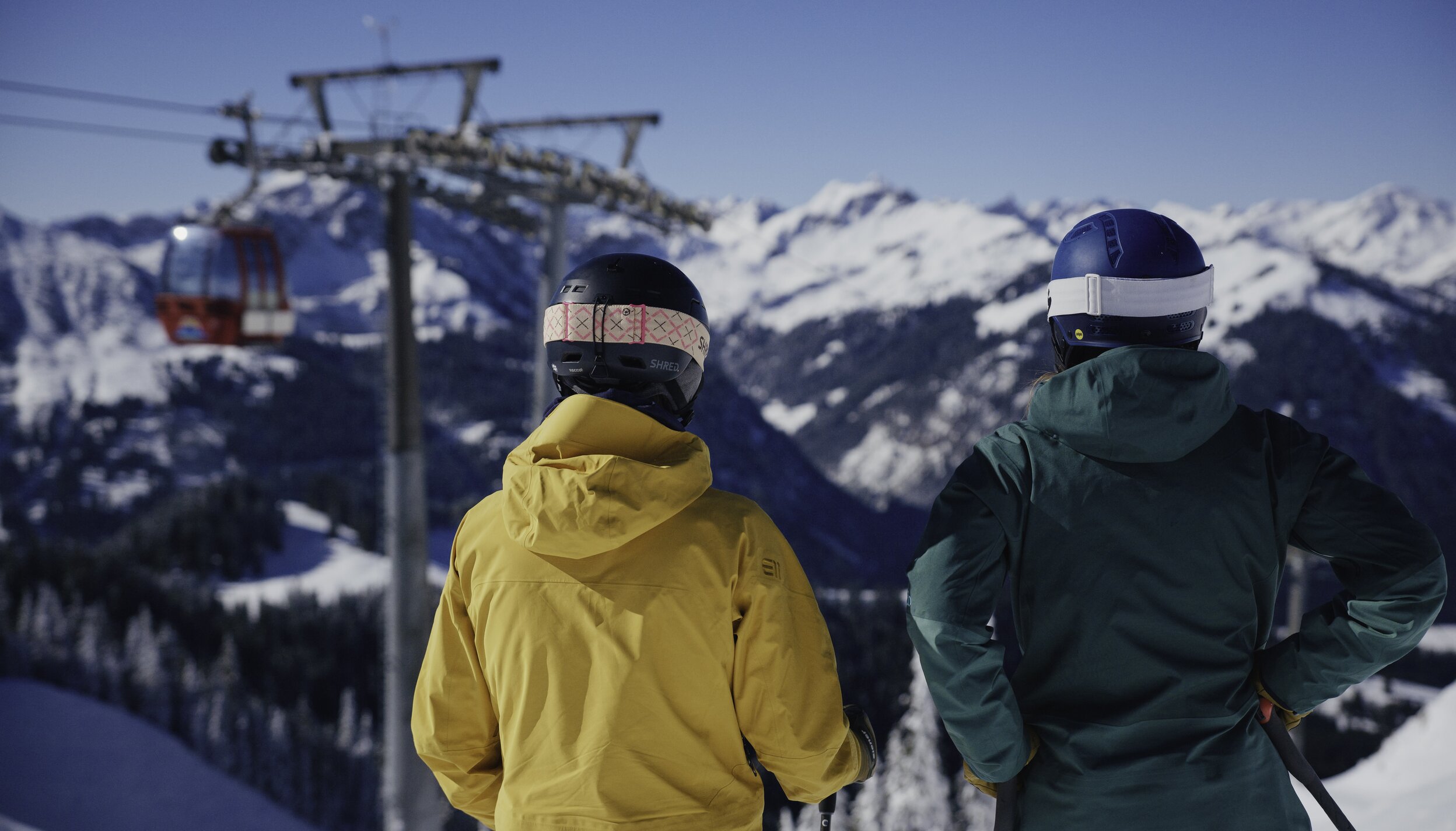 Zwei Skifahrer blicken auf verschneite Berge und Gondel