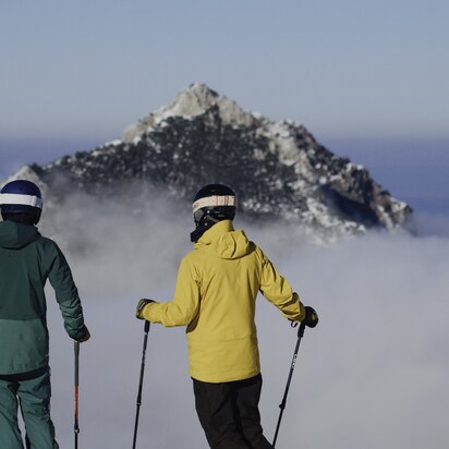 Skifahrerpaar vor schneebedecktem Berg über Wolkenmeer
